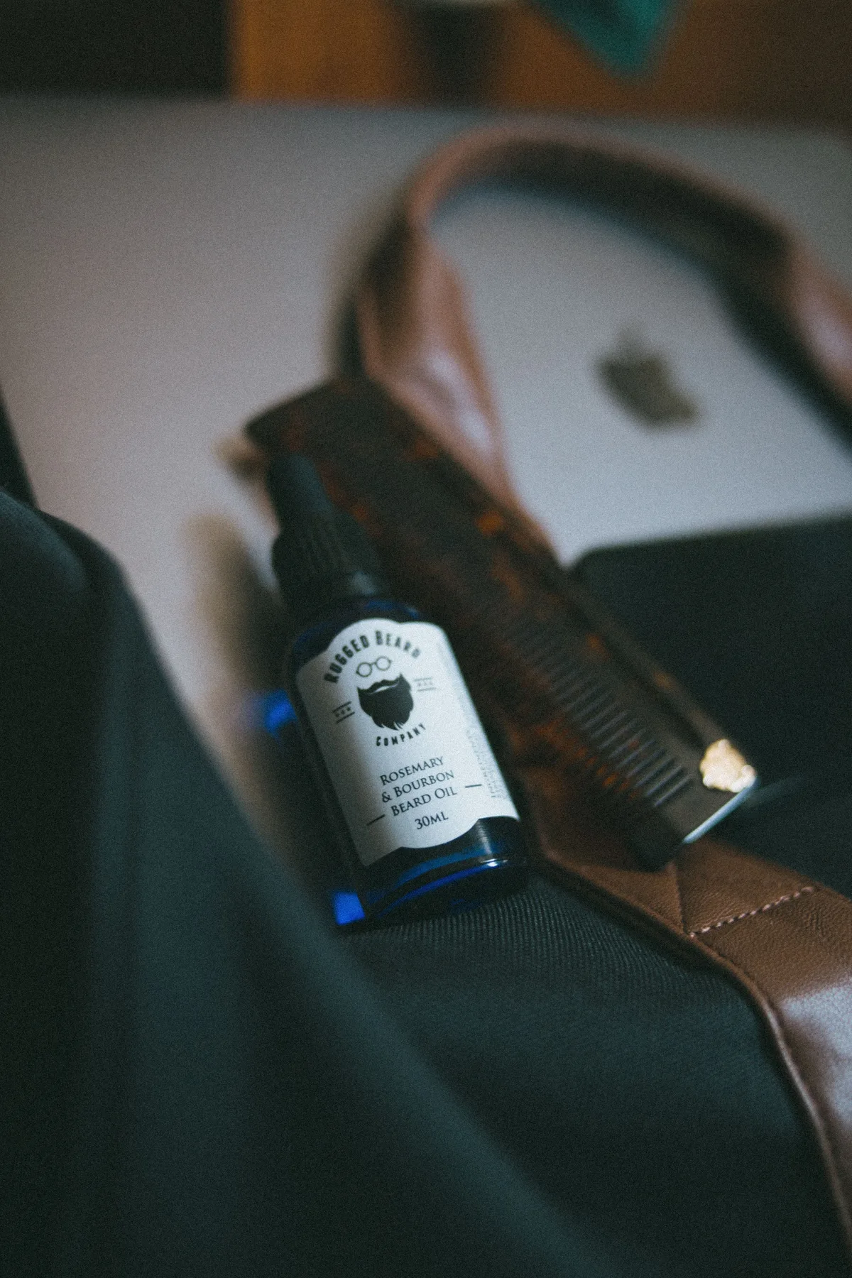 A beard oil bottle and comb arranged on a leather bag